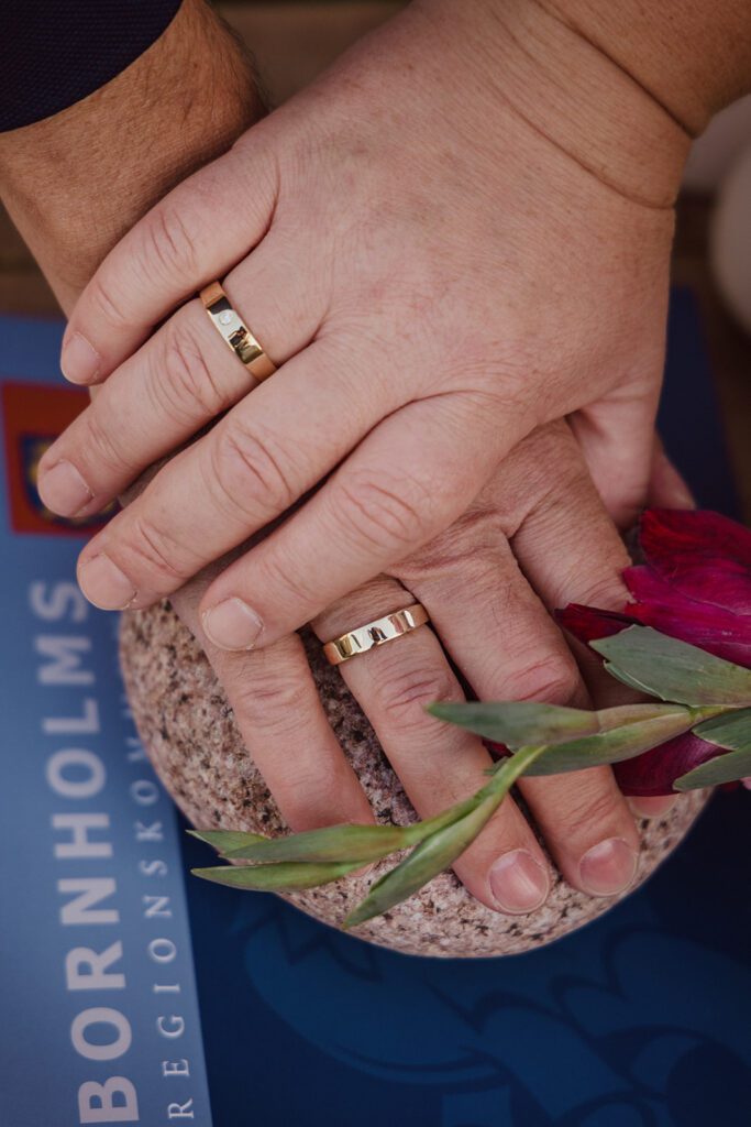 A just married couple crosses their hands on a wedding stone displaying their wedding bands on Bornholm.