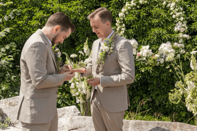 Männliches homosexuelles Paar heiratet vor Blumenschmuck an einem Strand in Bornholm.