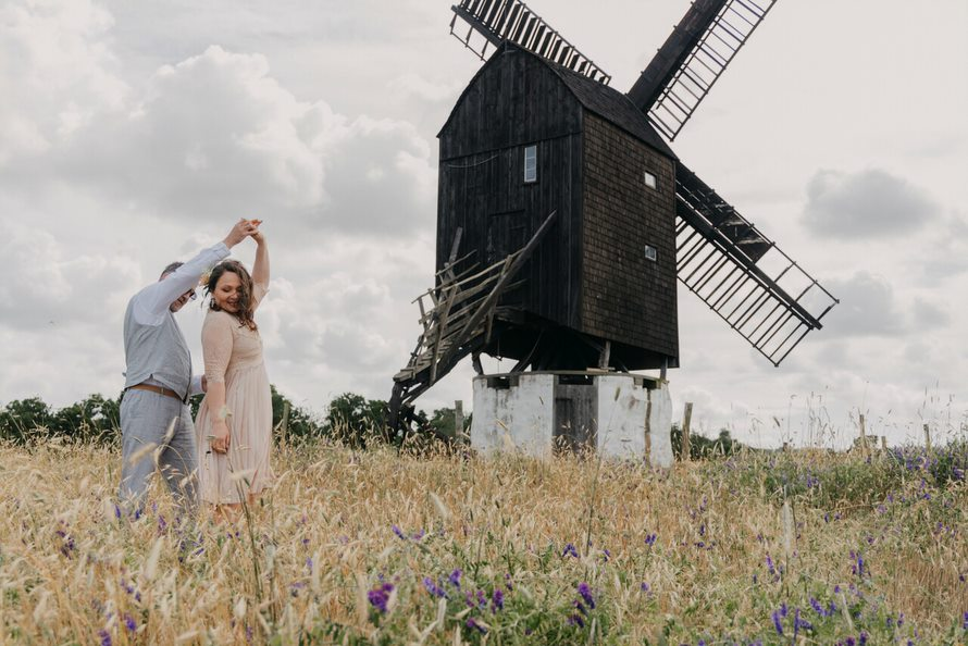 Ein Hochzeitspaar auf einem Feld auf Bornholm mit einer Mühle im Hintergrund.