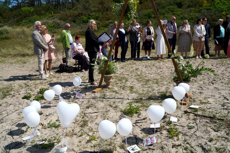 A large group of wedding guests watch a same sex female couple walk down the aisle on Klympen Beach in Bornholm.