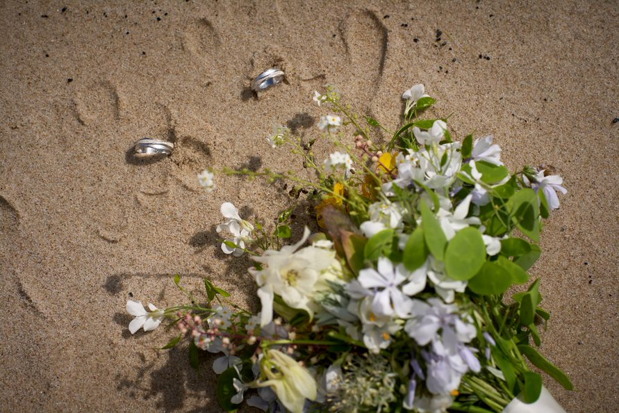 Der Brautstrauß und die Eheringe liegen auf einem Sandstrand auf Bornholm in Dänemark als Teil des Hochzeitsfotoshootings.