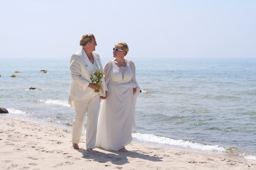 Ein frisch verheiratetes lesbisches Paar spaziert nach einer Strandhochzeit den Strand entlang, an dem es in Dänemark geheiratet hat.