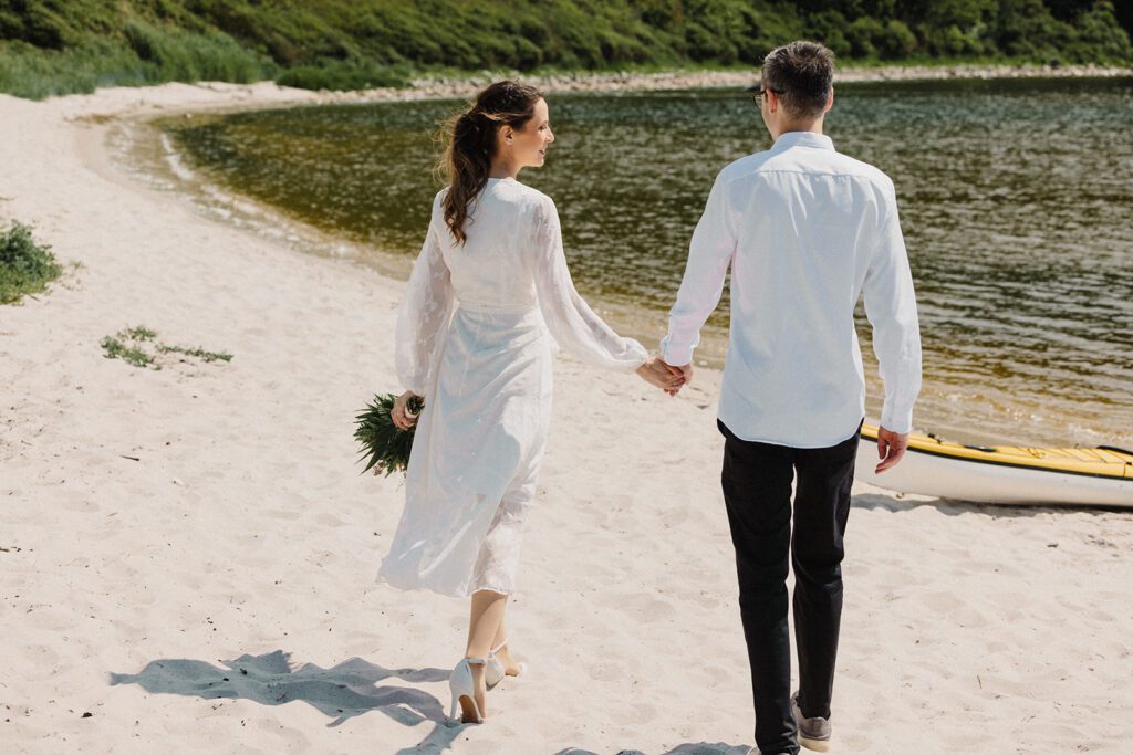 Bride and groom walk on the beach at Hammershus Harbour on the island of Bornholm in Denmark.