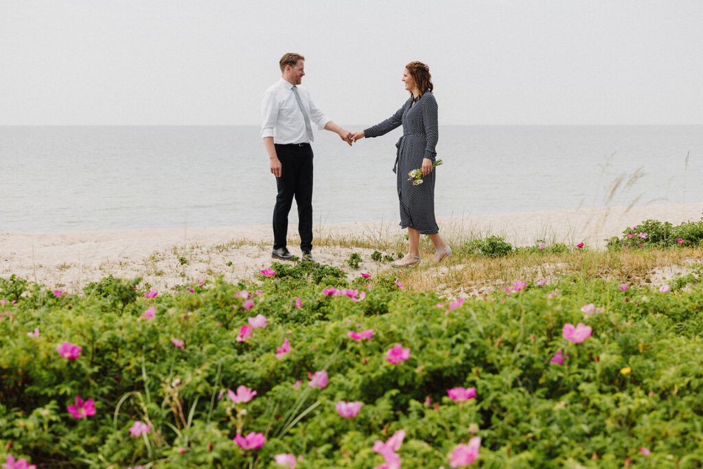 Ein frisch verheiratetes deutsches Paar hält am Strand von Bornholm Händchen nach ihrer Blitzhochzeit.