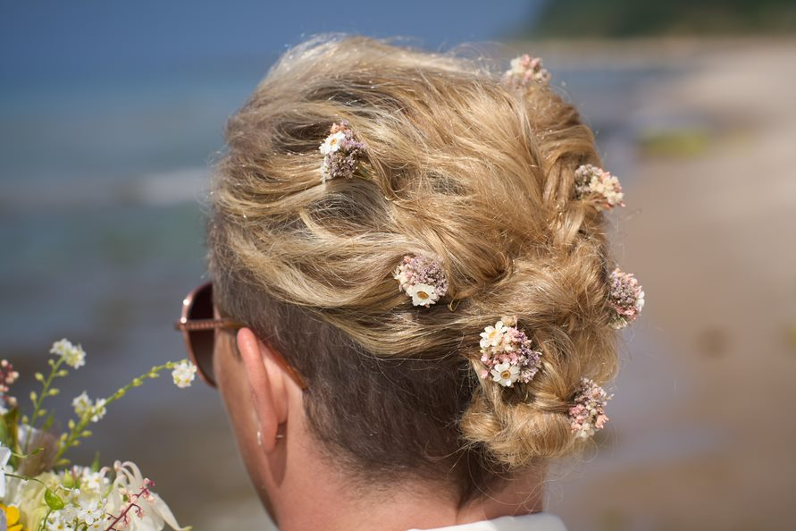 Blumen als Teil der Hochzeitsfrisur einer Braut kurz vor ihrer Strandhochzeit auf Bornholm in Dänemark.