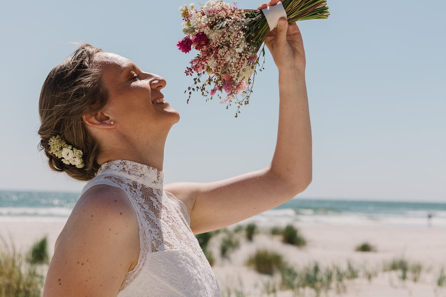 Eine Braut nach einer Strandhochzeit auf Bornholm mit angepasster Hochzeitsfrisur, Make-up und Brautstrauß.