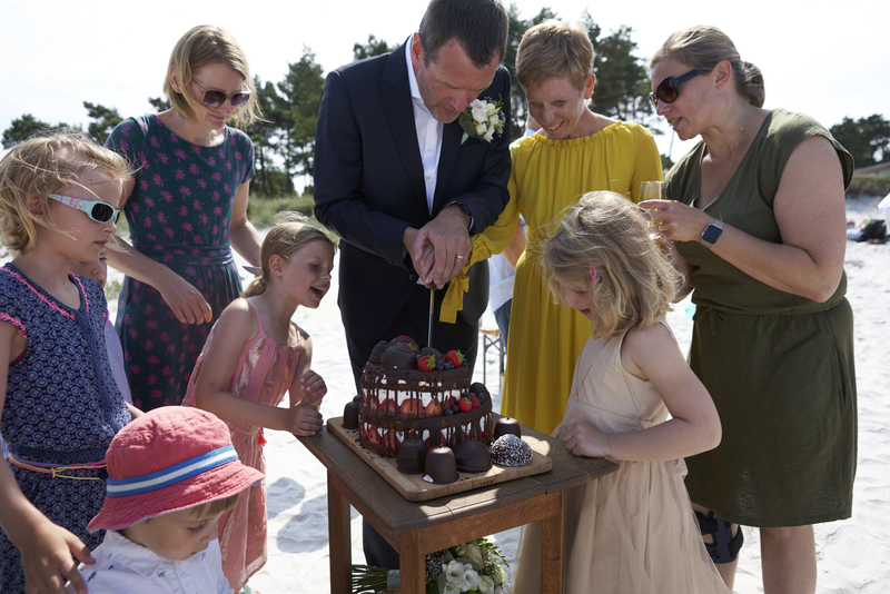 Wedding guests surrounding a wedding cake during a beach wedding in Denmark.