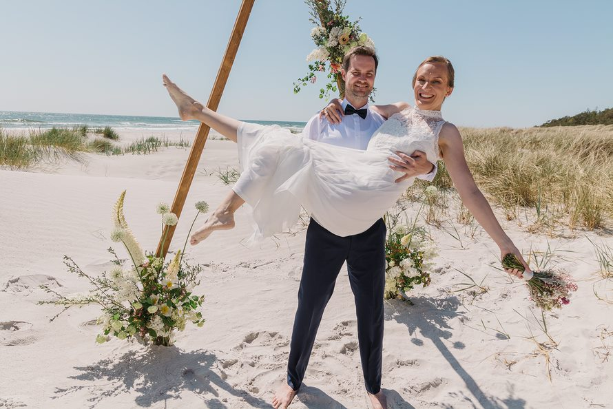 Ein Bräutigam trägt seine Braut auf den Armen am Strand von Bornholm in Dänemark.