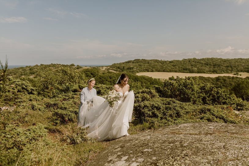 Eine dänische Hochzeitsplanerin hilft der Braut beim Aufstieg auf einen Hügel auf Bornholm.