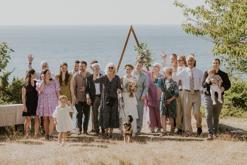 Eine große Gruppe von Hochzeitsgästen posiert an einem Strand auf Bornholm für den Hochzeitsfotografen.